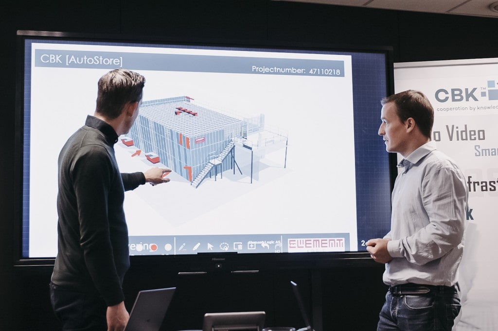 Two men are pointing and looking at a presentation of a drawing of an AutoStore solution.